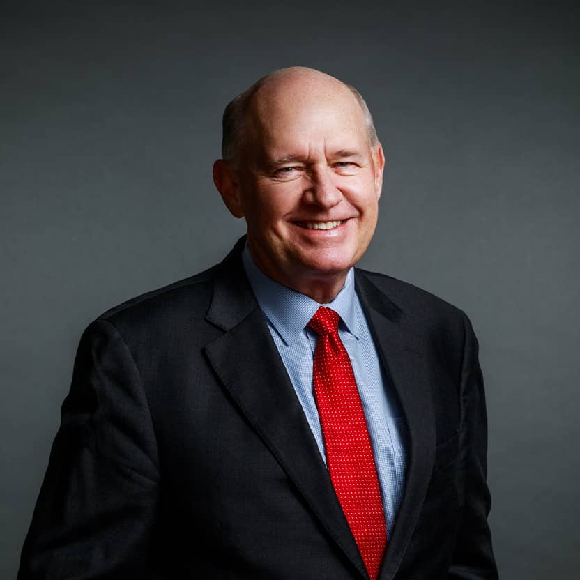 A man wearing a black suit, blue shirt, and red necktie